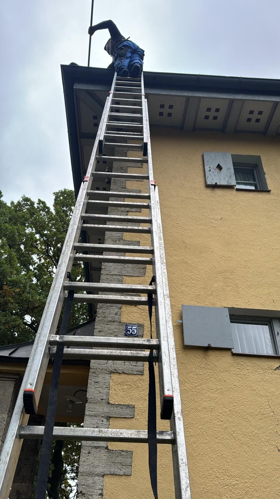Dachrinnenreinigung auf einer hohen Leiter